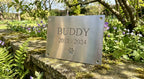 The Forever Paw stainless steel pet memorial plaque with engraved name and paw print, sitting in a garden setting